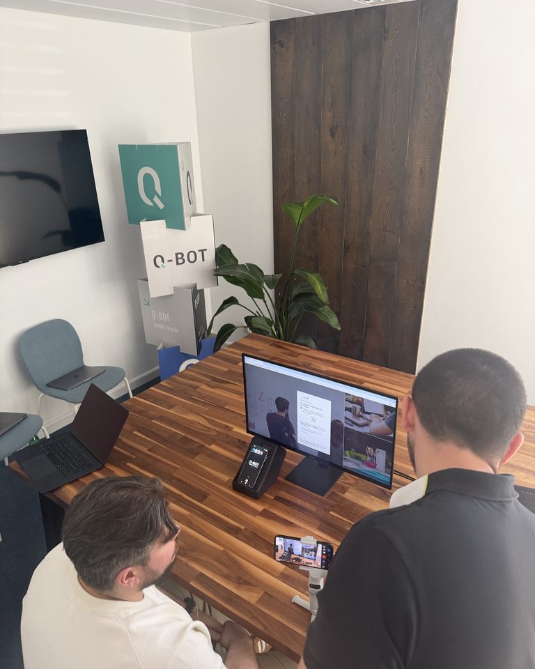 Deux membres de l'équipe Q-Leap en visioconférence dans la salle de réunion, à côté du kakemono Q-Bot